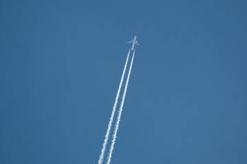 Airplane flying at high altitude leaving its white wake over blue sky