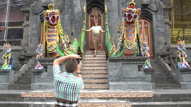 A man takes pictures of a woman on a smartphone in front of the entrance to a Buddhist temple