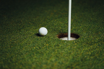 golf ball nearby hole with pin flag, green grass background, closeup view