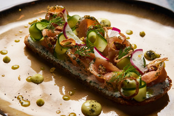 Danish smorrebrod sandwich with salmon fish, curd mousse, marinated cucumber and radish. Delicious vegetarian snack food with dark rye bread and different topping on plate at restaurant table