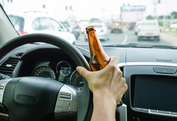 A driver holding alcoholic bottle while driving / Drunk driving concept