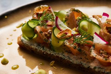 Smorrebrod Danish sandwich with salmon fish, curd mousse, marinated cucumber and radish. Delicious vegetarian snack food with dark rye bread and different topping on plate at restaurant table top view