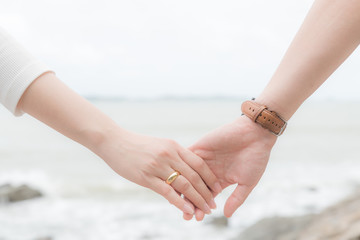 Symbols of love. Couple of man and woman hand holding together on blurred sea and sky background for love and valentines day concept