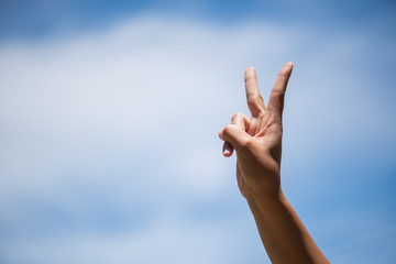 Woman hand showing two fingers as victory sign on blue sky with white cloud background