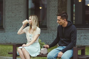 man pickpocketing smartphone from bag of woman drinking coffee to go on bench in park
