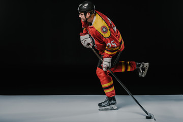 side view of young sportsman playing ice hockey on black