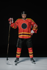 Fototapeta premium full length view of professional ice hockey player standing with hand on waist and looking at camera on black
