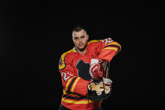 Handsome Professional Ice Hockey Player Standing With Sports Equipment And Looking At Camera Isolated On Black