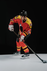 full length view of professional sportsman playing hockey and looking away on black