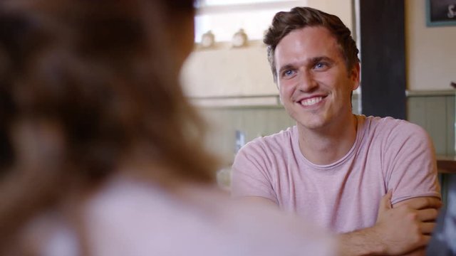Attractive young male flicks his hair as he talks to a  woman on a date in a coffee shop