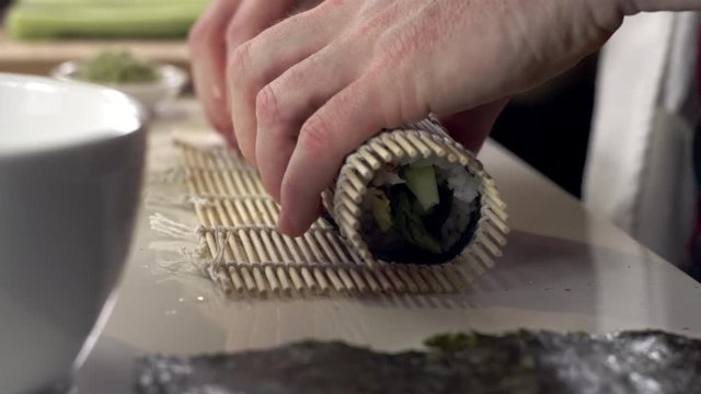 Sushi chef using bamboo mat to make fresh sushi roll