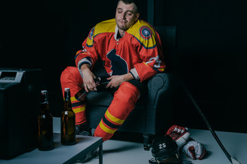 young hockey player drinking beer and watching tv while sitting in armchair in black