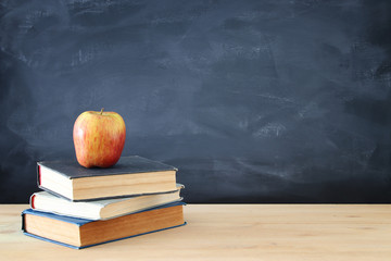 back to school concept. stack of books over wooden desk in front of blackboard.