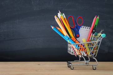Shopping cart with school supply in front of blackboard. Back to school concept. © tomertu