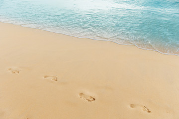 Fototapeta na wymiar sand beach leaving footprints in the sand. Closeup detail of female feet and golden sand