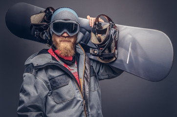 Portrait of a snowboarder dressed in a full protective gear for extream snowboarding posing with a snowboard on his shoulder at a studio. Isolated on gray background.