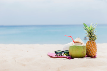 Fresh young coconut and pineapple lying on the sand beach background with straw ready for drink. Tropical vacation travel concept