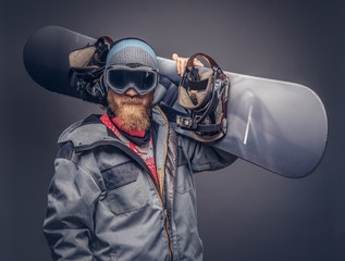 Portrait of a snowboarder dressed in a full protective gear for extream snowboarding posing with a snowboard on his shoulder at a studio. Isolated on gray background.