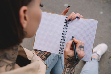 selective focus of tattooed young woman writing in empty textbook