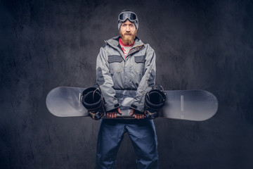 Brutal redhead snowboarder with a full beard in a winter hat and protective glasses dressed in a...