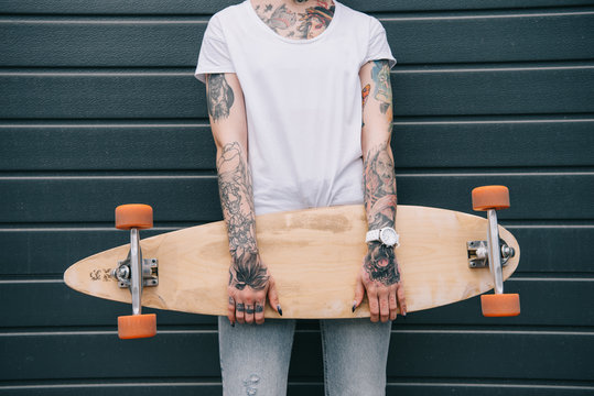 cropped image of woman with tattoos holding skateboard against black wall