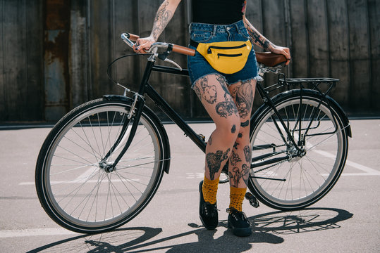 cropped image of stylish tattooed girl with waist bagstanding with bicycle at street