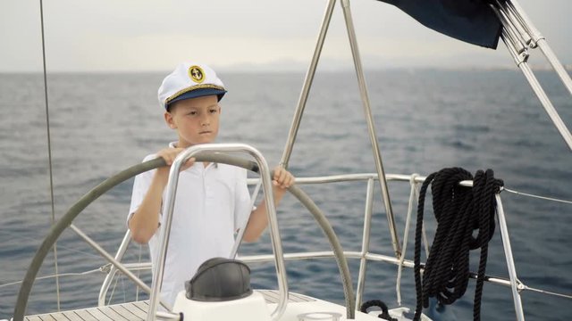 Litle children skipper at the helm controls of a sailing yacht during race.