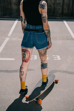 cropped image of stylish tattooed girl skateboarding at parking lot