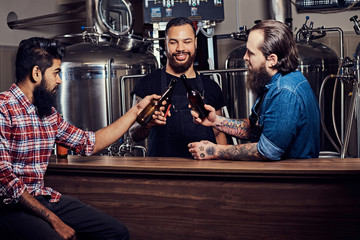 Three bearded interracial friends drink craft beer in a brewery.
