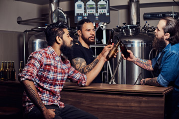 Three bearded interracial friends drink craft beer in a brewery.