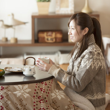 こたつでお茶を飲み微笑む女性