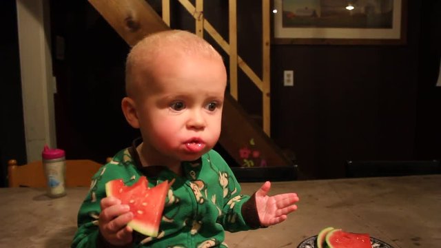 Pajama wearing toddler eats a watermelon in the night. The child wanted a late night snack, so he chose fruit.
