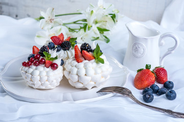 Delicate white meringues with fresh berries on the plate on white background. Dessert Pavlova. Wedding cake.