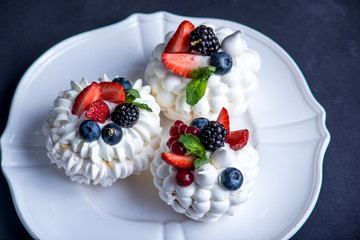 Delicate white meringues with fresh berries on the plate. Dessert Pavlova. Dark background. Wedding cake.