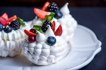 Delicate white meringues with fresh berries on the plate. Dessert Pavlova. Dark background. Wedding cake.