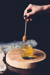 cropped image of woman putting honey stick into glass with honey on black background