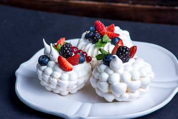 Delicate white meringues with fresh berries on the plate. Dessert Pavlova. Dark background. Wedding cake.