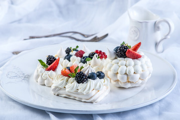 Delicate white meringues with fresh berries on the plate on white background. Dessert Pavlova close-up. Wedding cake.