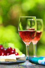 Two glasses of Shinning Rose Wine on wooden table with fresh Grapes and Cheese, bright and green outdoors background 2