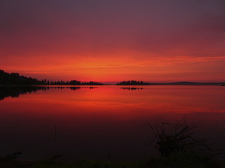 Summer landscape: the early dawn over the lake is very bright red, orange, like a fire