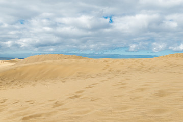 View of Dunes in Maspalomas, Canarias islands, Spain. Yellow and golden sand from Sahara desert and distance view of blue Atlantic ocean and beach.