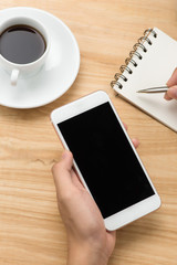Man hand holding smart phone and pen with white blank empty screen on white desk table.Business concept.
