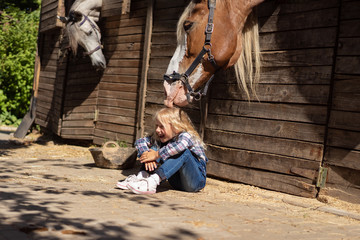 smiling kid sitting on ground and horse touching her hair at farm © LIGHTFIELD STUDIOS