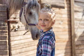 smiling kid palming white horse at farm and looking at camera