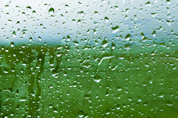 Natural background Drops on both sides of the glass from the rain and from the fogging abstract view, raindrops against the blue glass and the blurred landscape of the gradient of blue and green