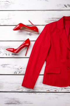 Red female suit jacket and high heel shoes. Vertical cropped view. Flat lay, bright wooden desks surface background.