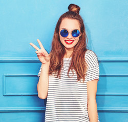 Young stylish girl model in casual summer clothes with red lips, posing near blue wall. Showing...