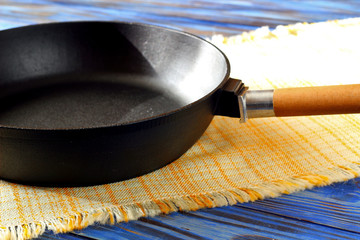 Empty vintage cast iron frying pan on checkered yellow kitchen towel on blue rustic wood background