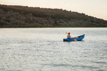 A young man is riding a kayak. Quiet waters and bright sun.