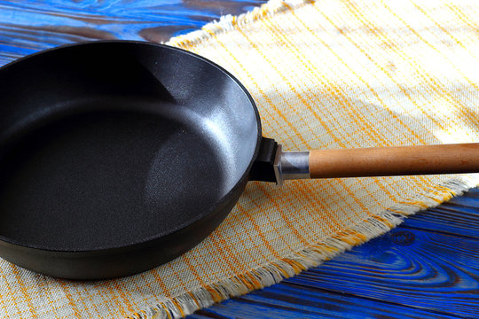 Empty vintage cast iron frying pan on checkered yellow kitchen towel on blue rustic wood background